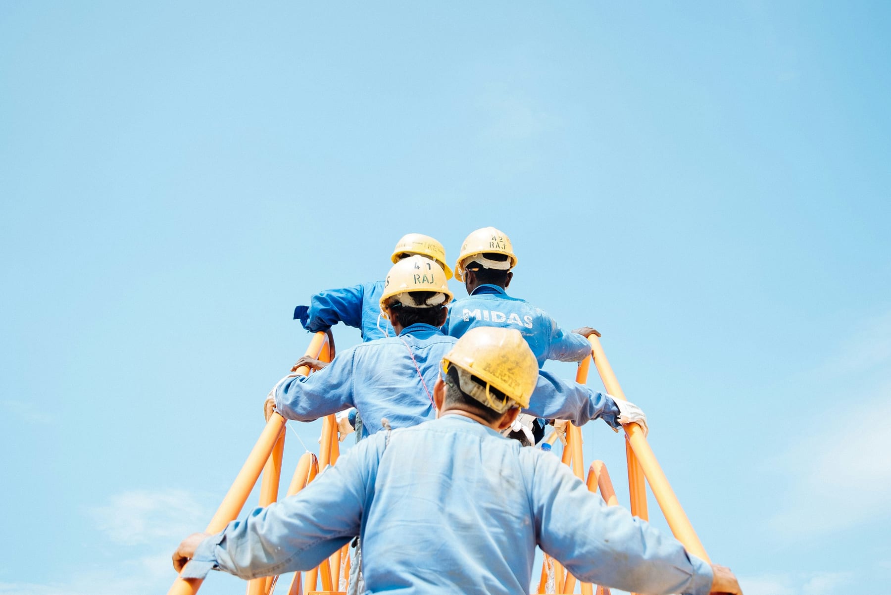 Three workers in hard hats climbing scaffolding against a clear sky