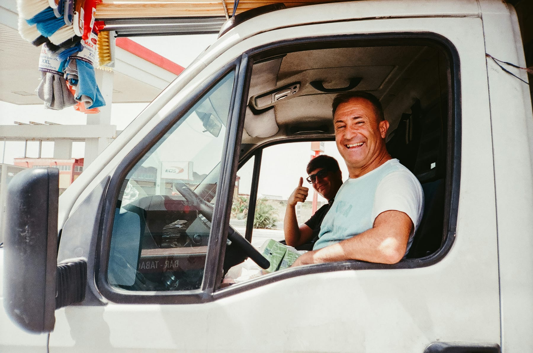 Two truck drivers smiling from the cab of their truck at a service station