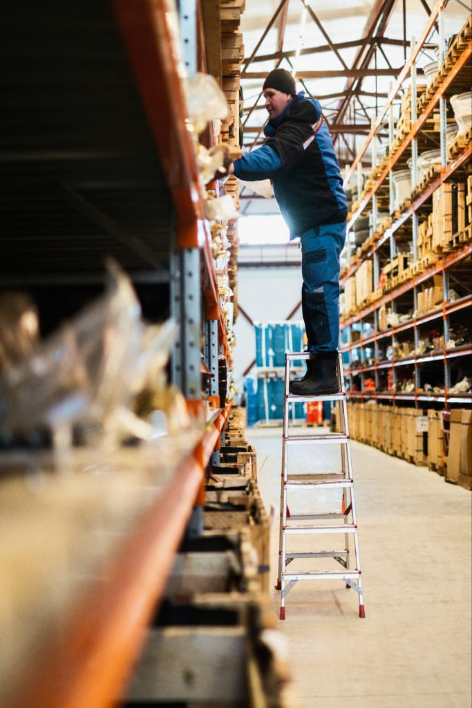 A warehouse worker on a step ladder picking stock from high pallet racking
